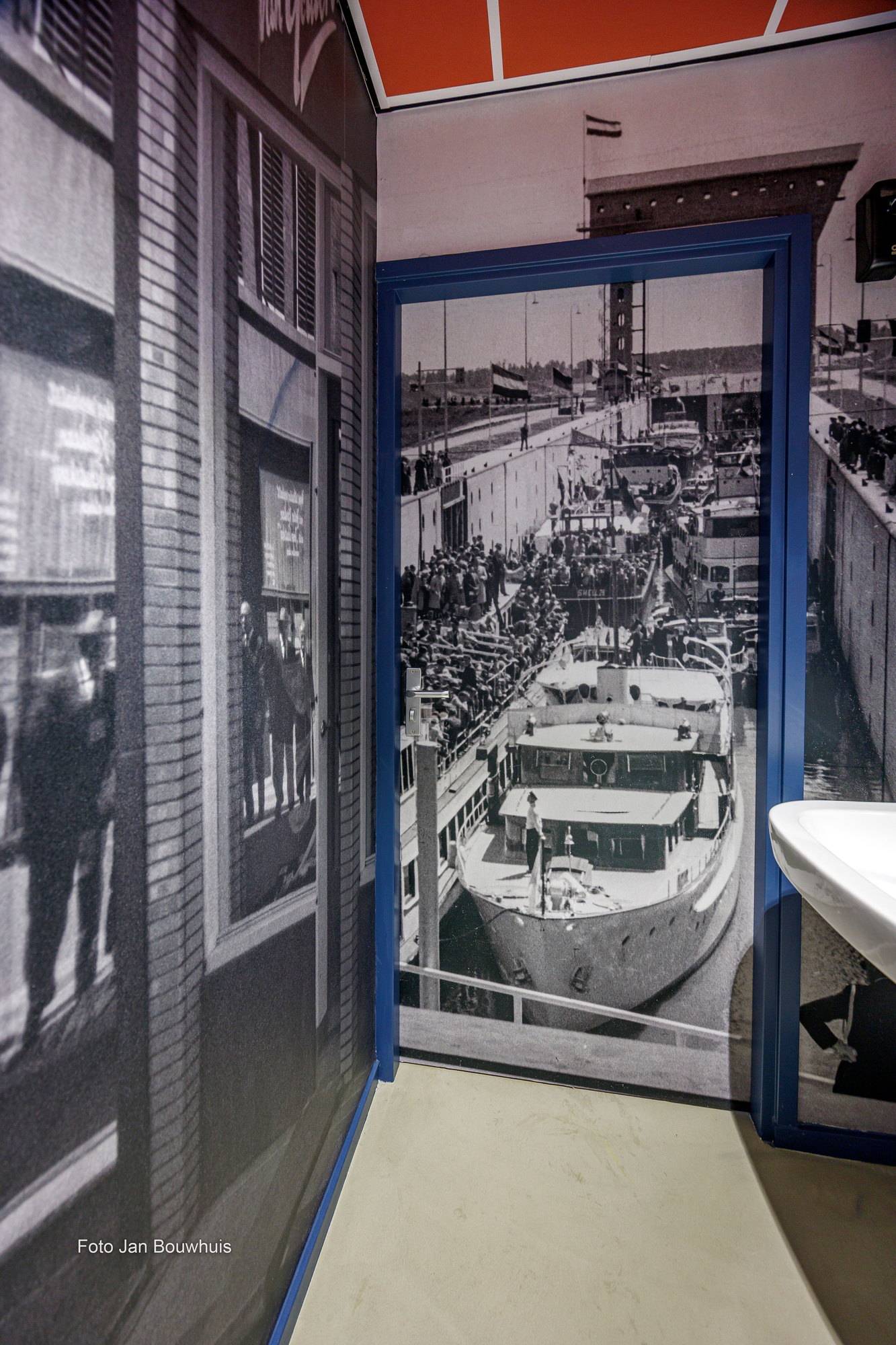Een deuropening met daarachter fotobehang van historische foto's met schepen en straten.