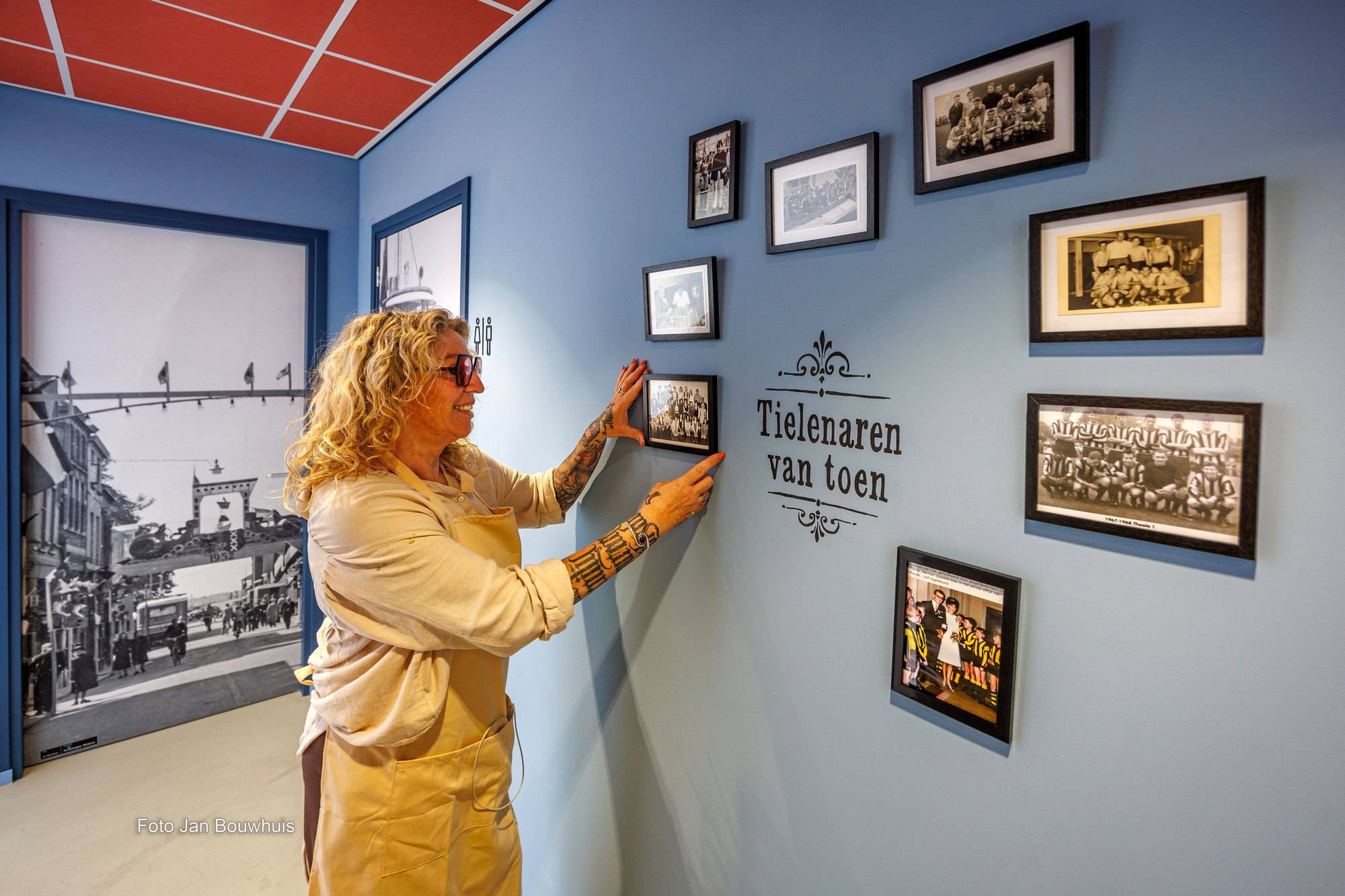 Een medewerkster hangt een foto op bij de wand Tielenaren van toen, met oude groepsfoto's.