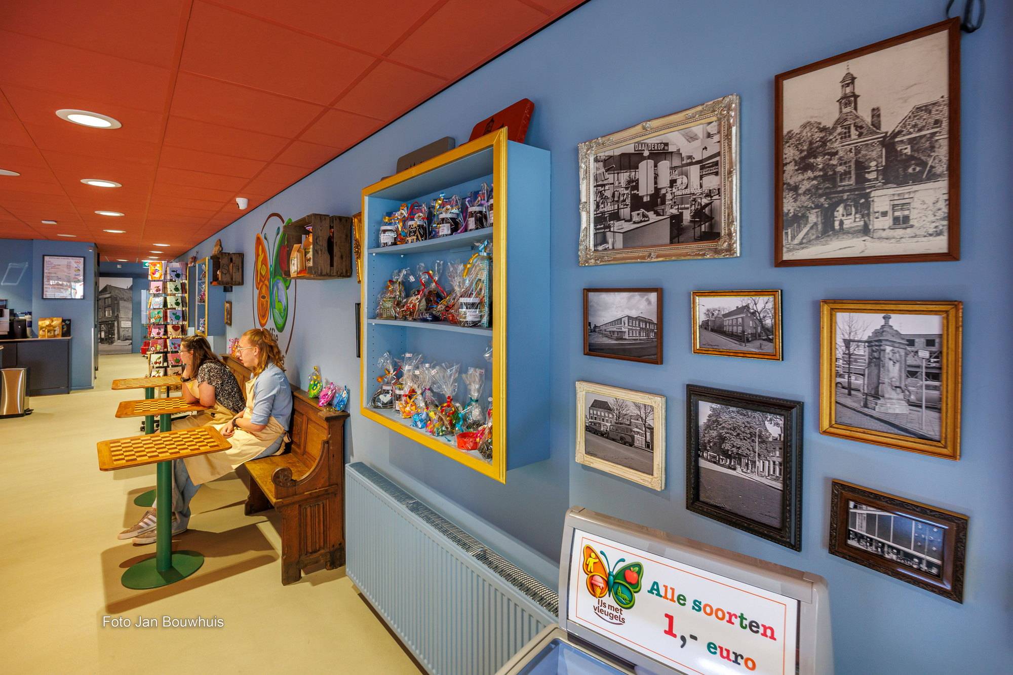 De wand met oude foto's van Tiel in lijsten, een vitrine met kado's en twee bezoekers op de kerkbank.