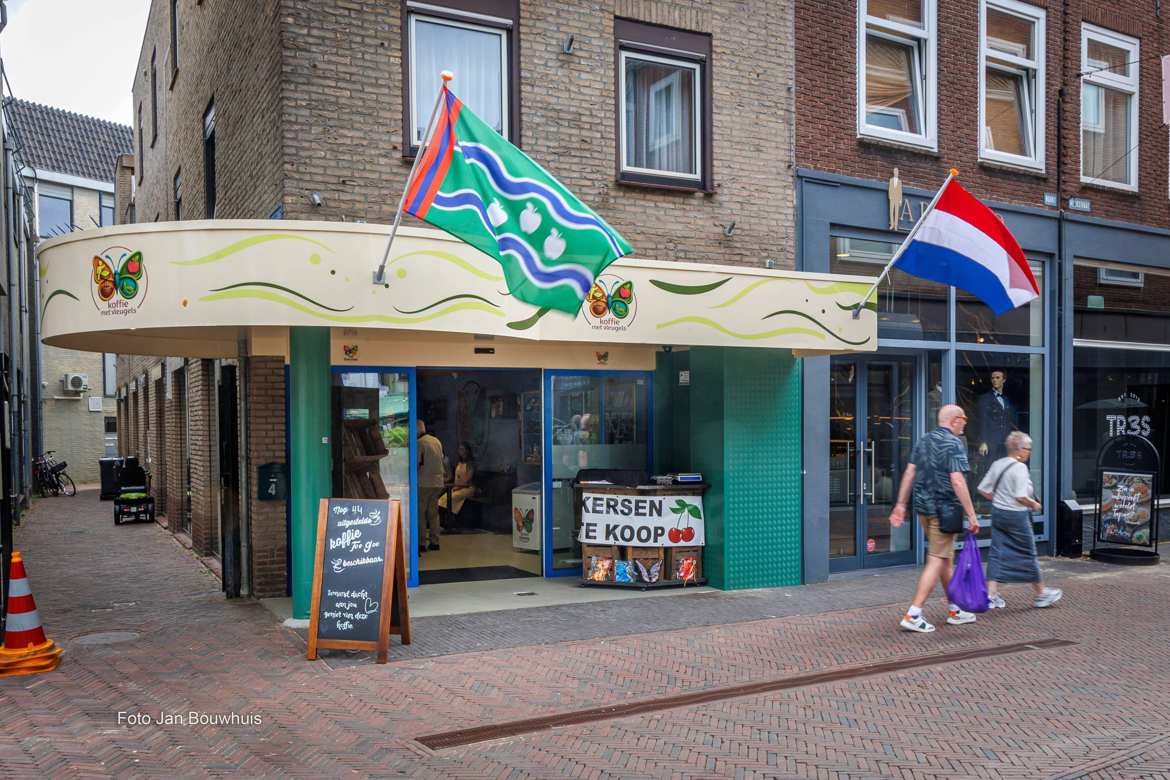 De gevel van Koffie met Vleugels aan de Markt in Tiel: een luifel met de vlinder, de Tielse vlag en de Nederlandse vlag, en een krijtbord op de stoep.