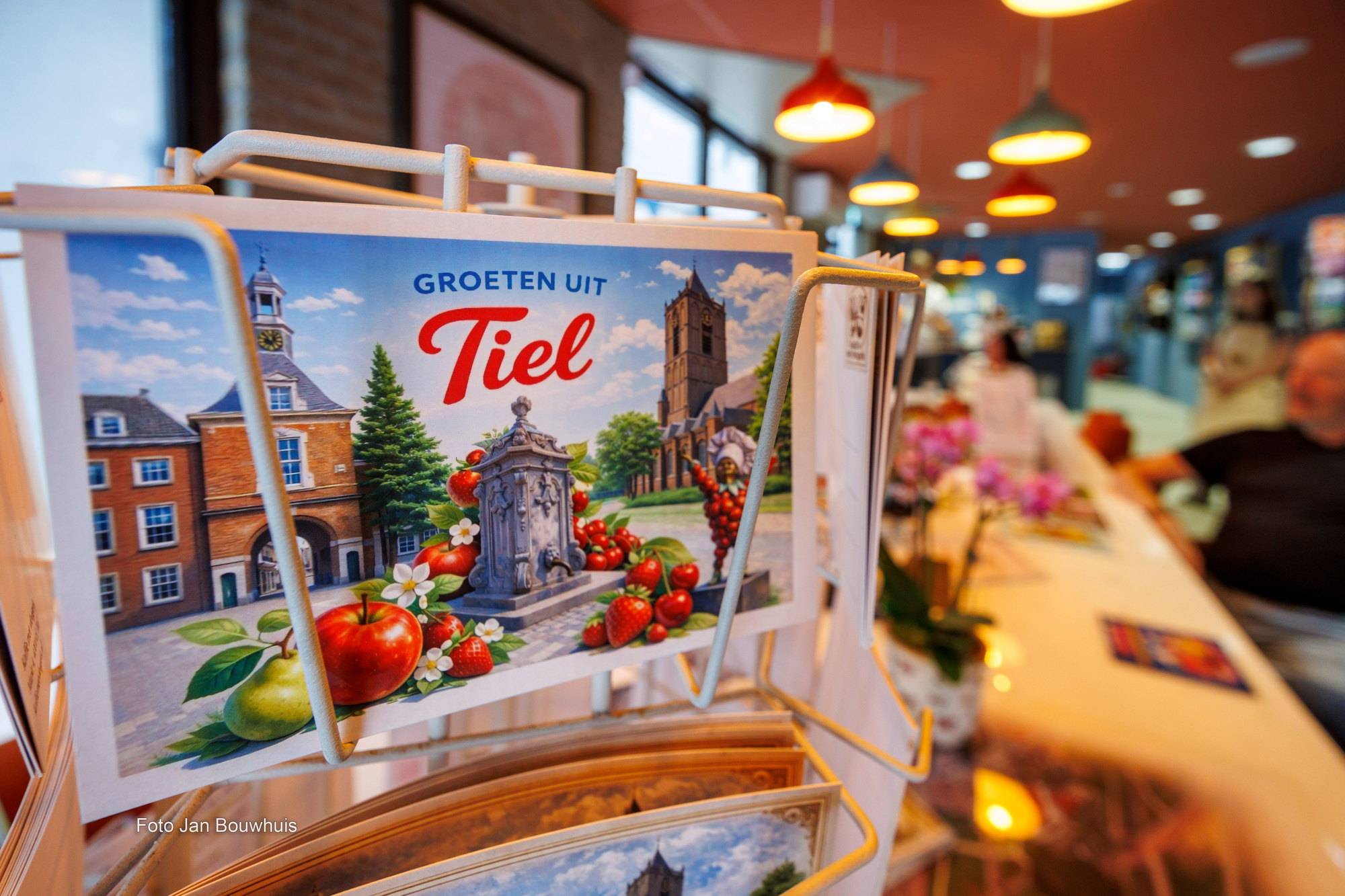 Een rek met ansichtkaarten Groeten uit Tiel in de koffiebar, met op de achtergrond bezoekers aan de tafel.